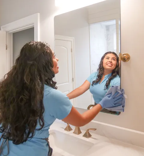 merry maid cleaning a bathroom mirror