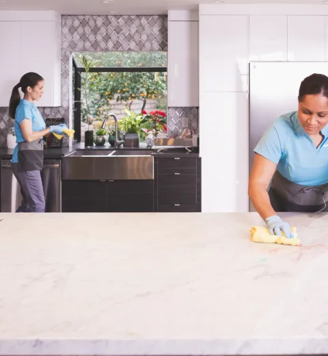 Merry Maids house cleaning team wiping down countertops in a modern kitchen.