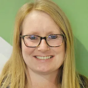 tami is wearing a blue merry maids tshirt standing in front of a green and white wall
