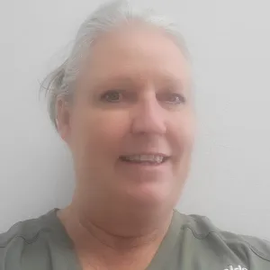 tammy is wearing a green merry maids uniform standing in front of a grey wall