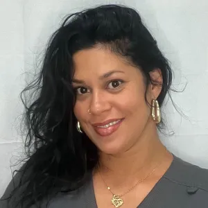 Anais is smiling standing in front of a grey wall wearing a grey merry maids uniform