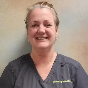 smiling woman with a grey merry maids uniform standing in front of a tan wall