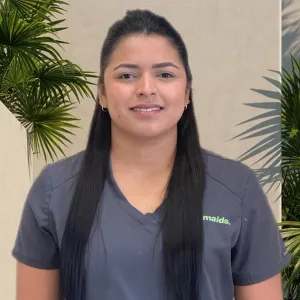 woman with long dark hair standing in front of a white wall with greenery