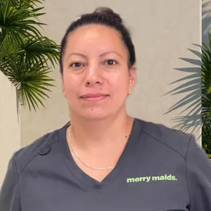smiling woman with a grey merry maids uniform standing in front of a tan wall