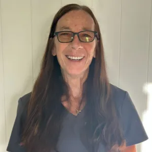 pam is wearing a grey merry maids uniform standing in front of a grey wall