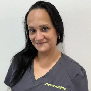 smiling woman with a grey merry maids uniform standing in front of a tan wall