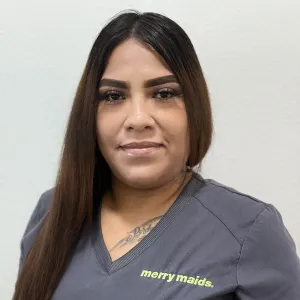smiling woman with a grey merry maids uniform standing in front of a tan wall
