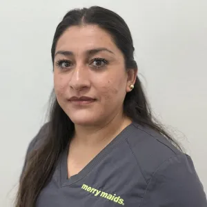 smiling woman with a grey merry maids uniform standing in front of a tan wall