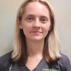 smiling woman with a grey merry maids uniform standing in front of a tan wall