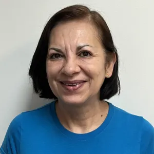 lily is smiling in front of a grey wall wearing a blue merry maids tshirt