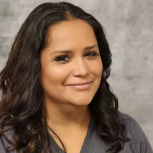 smiling woman with a grey merry maids uniform standing in front of a tan wall