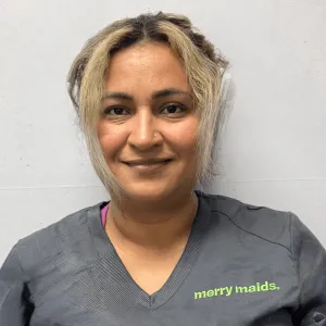 Sulma is smiling standing in front of a grey wall wearing a grey merry maids uniform