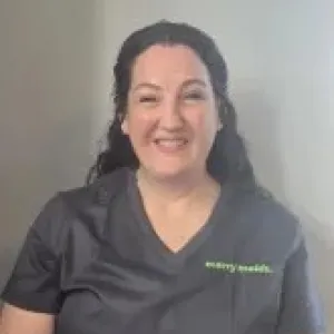 kelly is smiling in front of a grey wall wearing a merry maids uniform