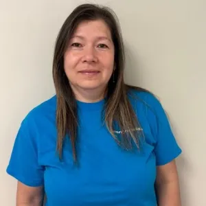 smiling woman with a blue merry maids uniform standing in front of a tan wall
