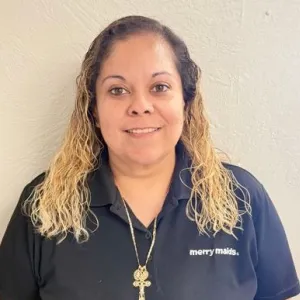 smiling woman with a blue merry maids uniform standing in front of a tan wall