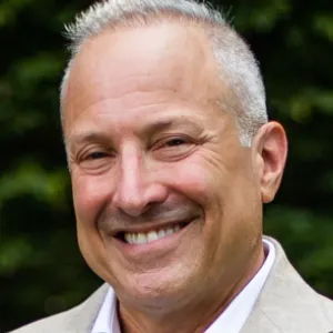 man with greying hair smiling in front of foliage