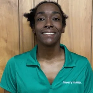 caress is wearing a green merry maids uniform shirt leaning against a wood paneled wall