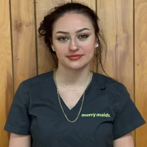 Sydney is wearing a grey merry maids uniform in front of a wood paneled wall