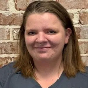 smiling woman with a grey merry maids uniform standing in front of a brick wall