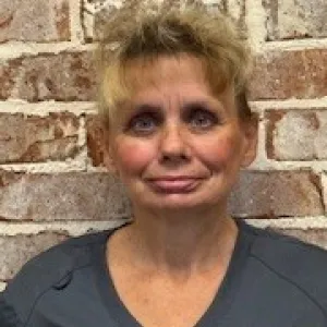 smiling woman with a grey merry maids uniform standing in front of a brick wall
