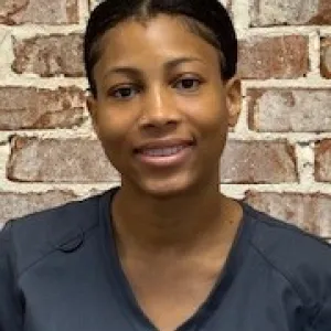 smiling woman with a grey merry maids uniform standing in front of a brick wall