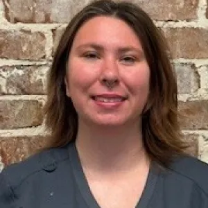 smiling woman with a grey merry maids uniform standing in front of a brick wall