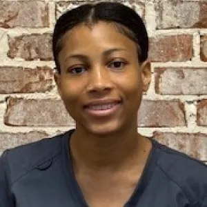 smiling woman with a grey merry maids uniform standing in front of a brick wall