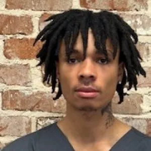 man wearing a grey merry maids uniform standing in front of a brick wall