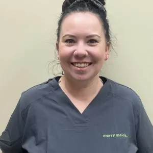 Smiling female in grey scrubs with Merry Maids logo with hair in a high bun