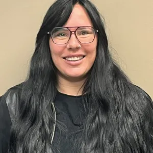 A smiling female Merry Maids ambassador in grey scrubs with long dark hair and glasses.