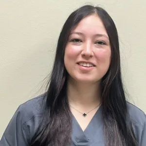 A smiling female Merry Maids ambassador in grey scrubs with long dark hair.
