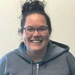 A smiling female Merry Maids ambassador in grey scrubs with dark hair styled in a high bun.