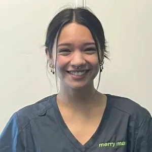 A smiling female Merry Maids ambassador in grey scrubs with dark hair styled in a high bun.