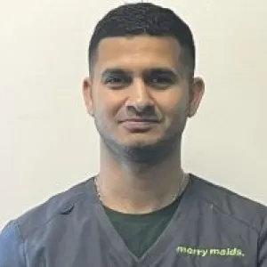 A smiling male Merry Maids ambassador in grey scrubs with dark short hair 