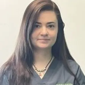 A smiling female Merry Maids ambassador in grey scrubs with dark shoulder length hair