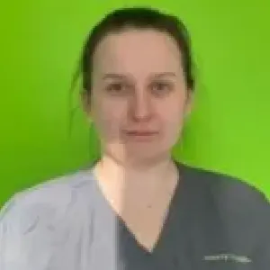 A smiling female Merry Maids ambassador in grey scrubs with dark hair pulled back