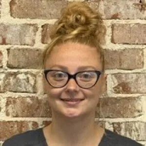 smiling woman with a grey merry maids uniform standing in front of a tan wall