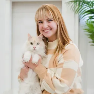 Kaylee is kneeling on a rug holding a white cat