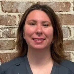 smiling woman with a grey merry maids uniform standing in front of a brick wall