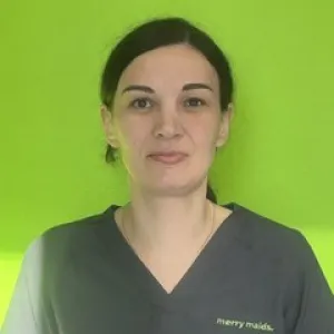 Smiling female in grey scrubs with Merry Maids logo with dark hair pulled back