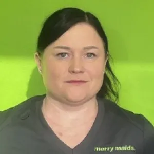 Smiling female in grey scrubs with Merry Maids logo with dark hair tied back