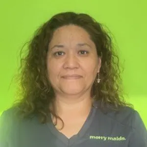 Smiling female in grey scrubs with Merry Maids logo with dark curly shoulder length hair.