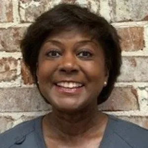smiling woman with a grey merry maids uniform standing in front of a tan wall