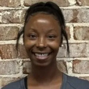 smiling woman with a grey merry maids uniform standing in front of a brick wall
