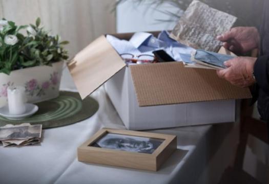 A close-up of a cardboard box being opened, revealing photos, letters, and other personal items. | Merry Maids