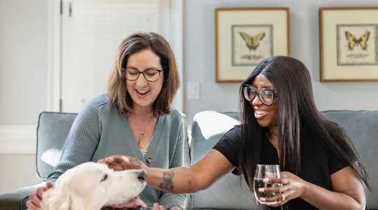 Two women on couch petting dog
