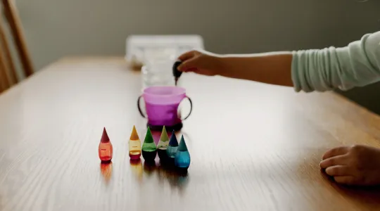 Child's arm reaching out to add drops of food coloring to a cup of water | Merry Maids