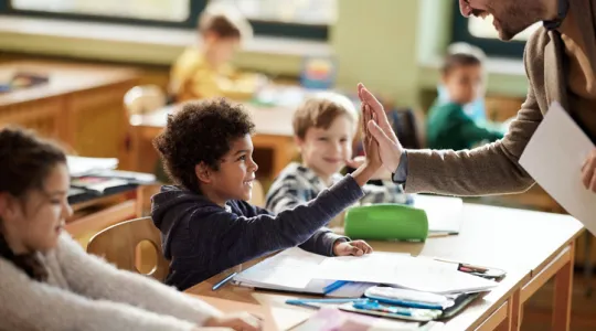 Happy male teacher giving a high-five to his black elementary student in the classroom | Merry Maids