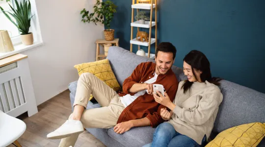 Young couple using smartphone device while relaxing on a sofa at home | Merry Maids