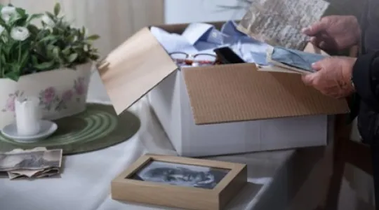 A close-up of a cardboard box being opened, revealing photos, letters, and other personal items. | Merry Maids